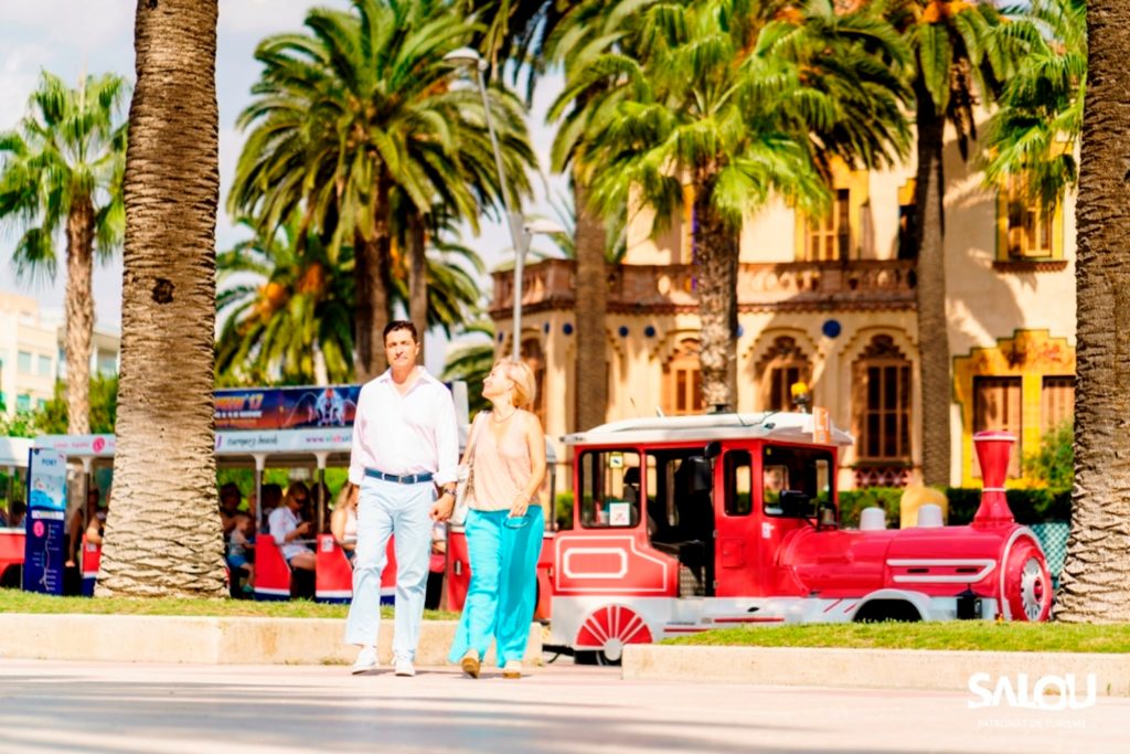 Couple walking along the promenade with the Salou tourist train behind.